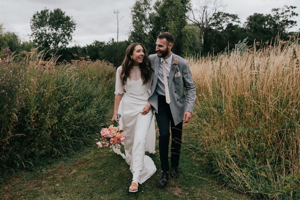 A couple walks through tall autumn grasses at sunset for an intimate outdoor photoshoot.