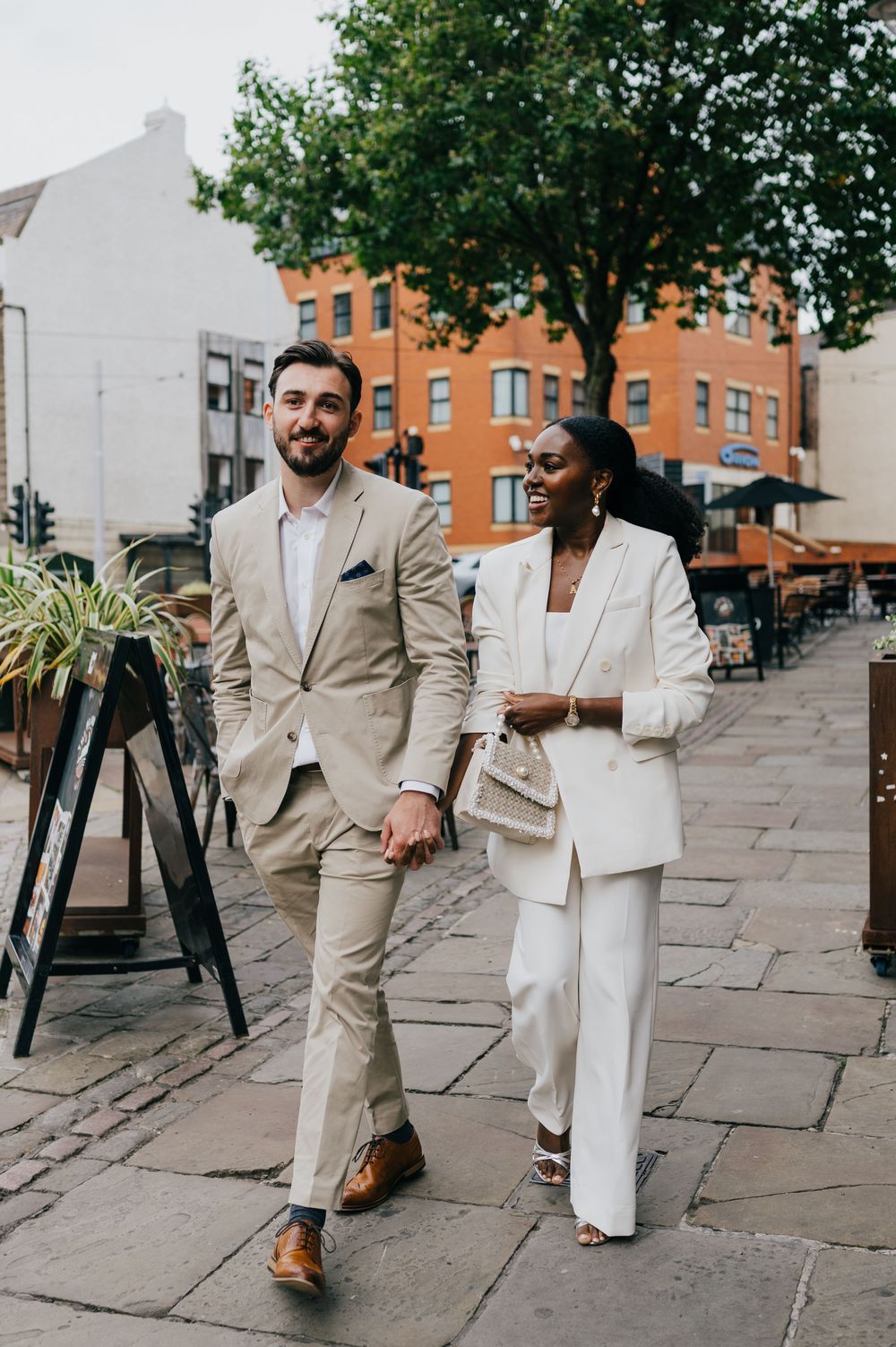 Two stylishly dressed professionals in coordinated cream and white suits walk together on a city sidewalk.