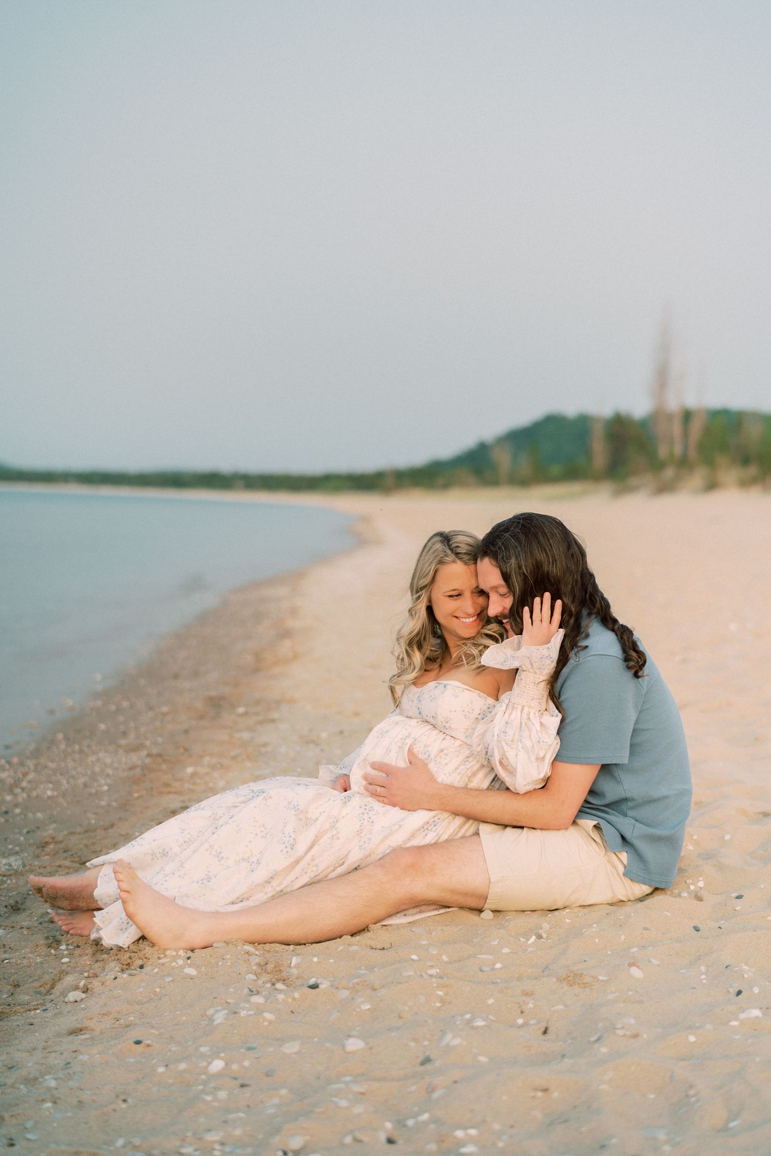 A couple in pastel colors lying together on a sandy beach at sunset creating a romantic seaside moment.