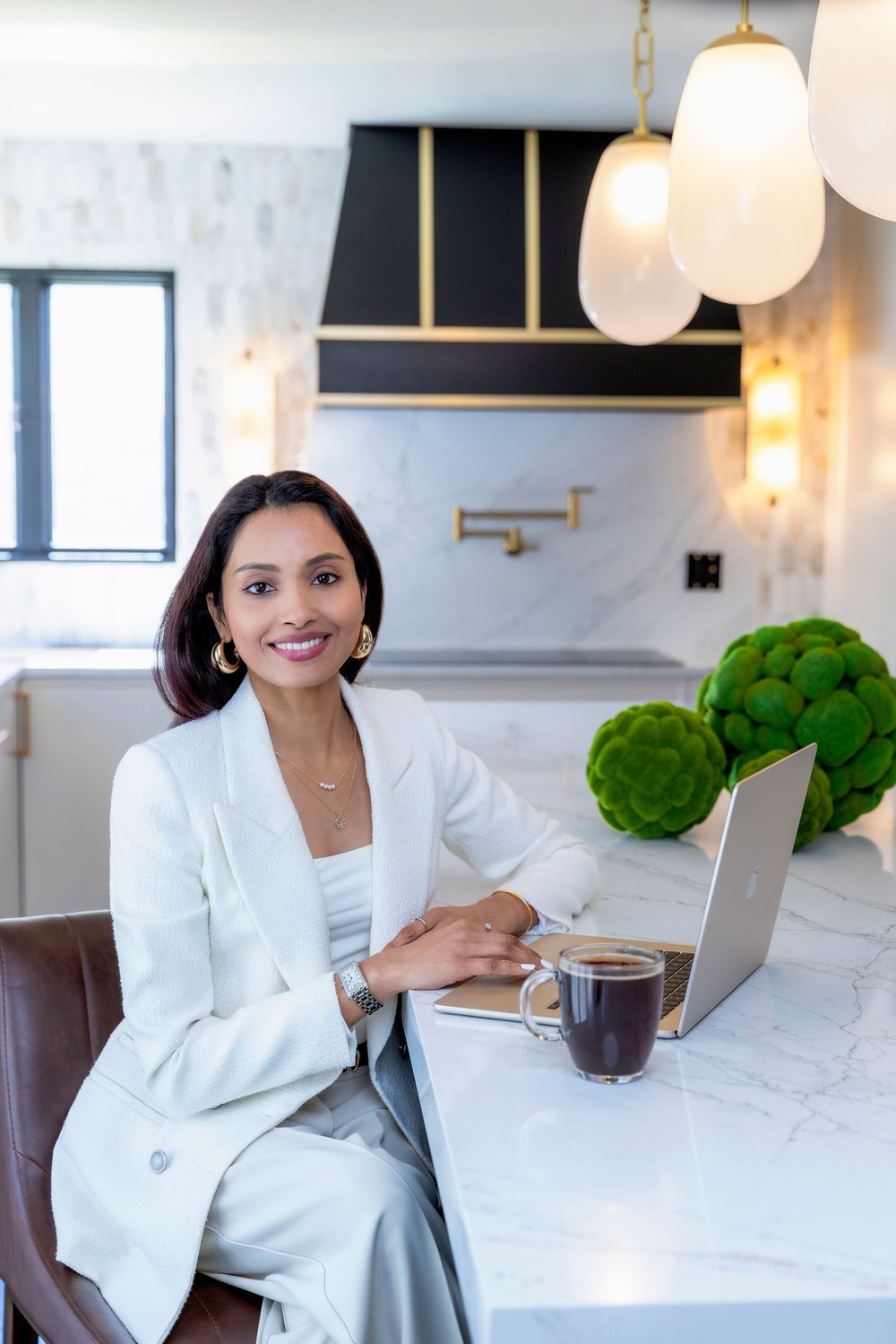 Professional working on laptop at modern marble kitchen counter with contemporary lighting and decor.