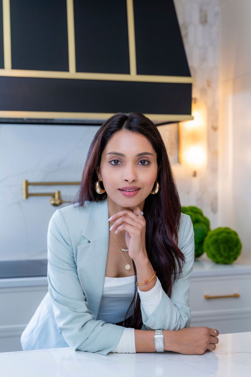 Professional portrait of someone in a light blue blazer seated at a modern desk with warm lighting and minimalist decor.