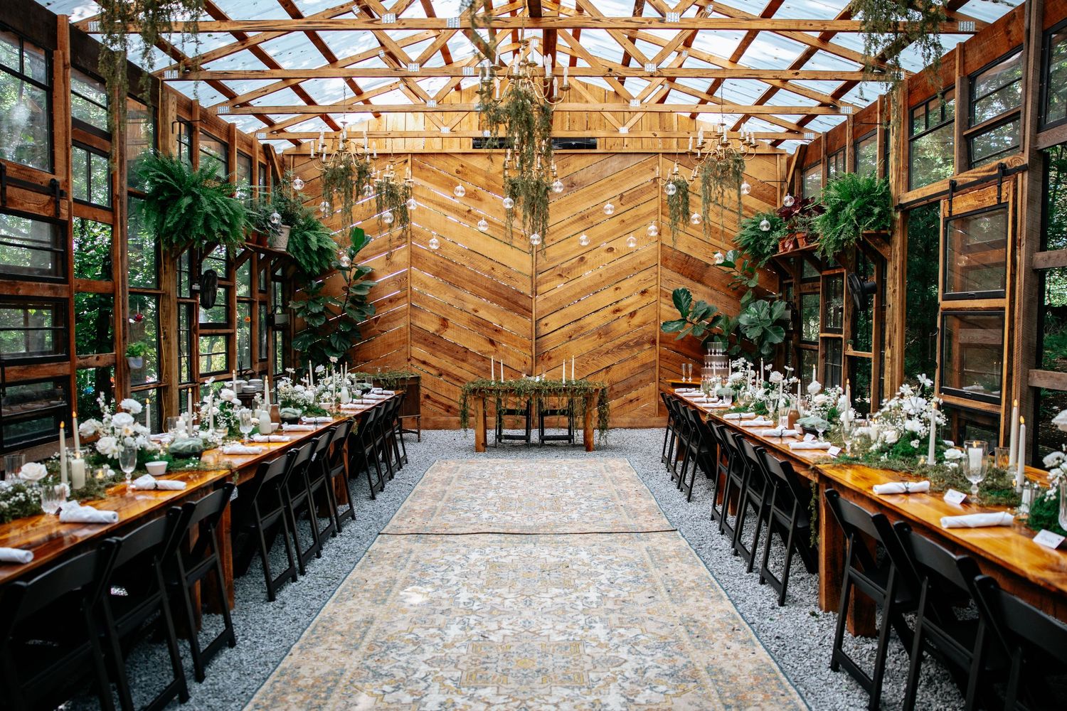 A rustic wooden barn venue with exposed beams and chandeliers set up for an elegant wedding reception.
