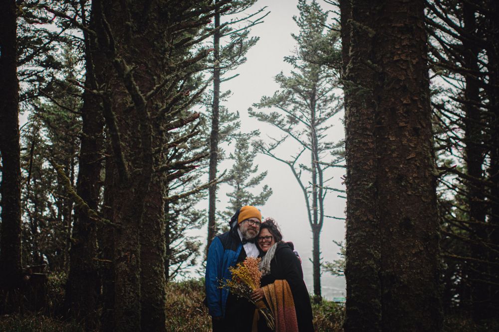 A romantic outdoor portrait between tall pine trees in moody lighting.
