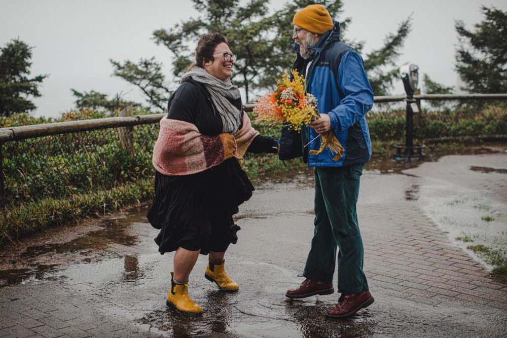 Two people share bright autumn flowers while standing in the rain.