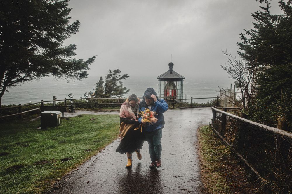 A couple embraces near a lighthouse on a foggy coastal path.
