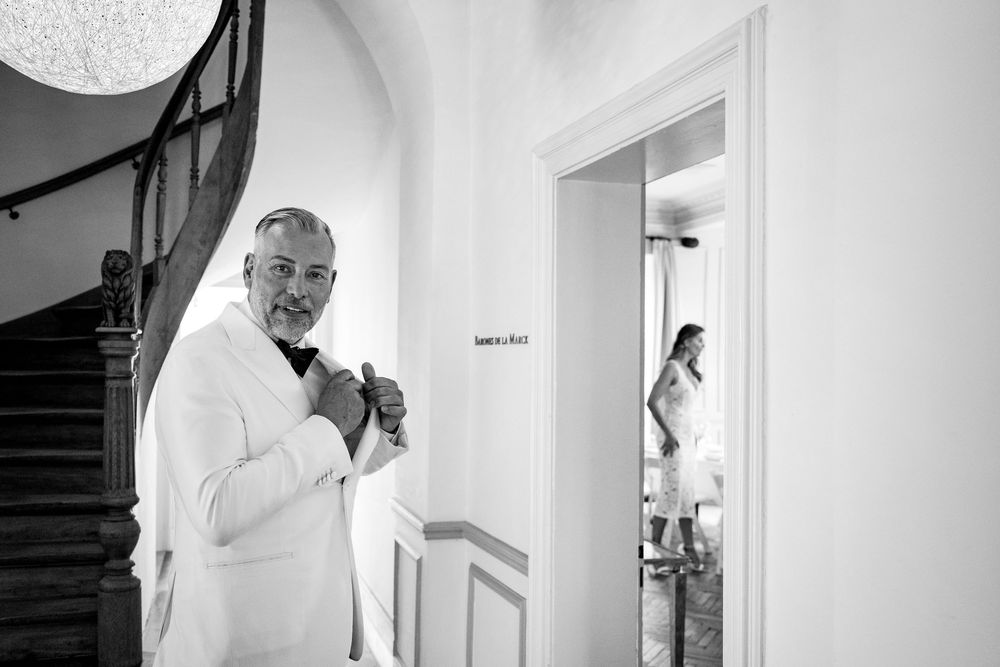 A person in white adjusts their bowtie while preparing for a wedding ceremony.
