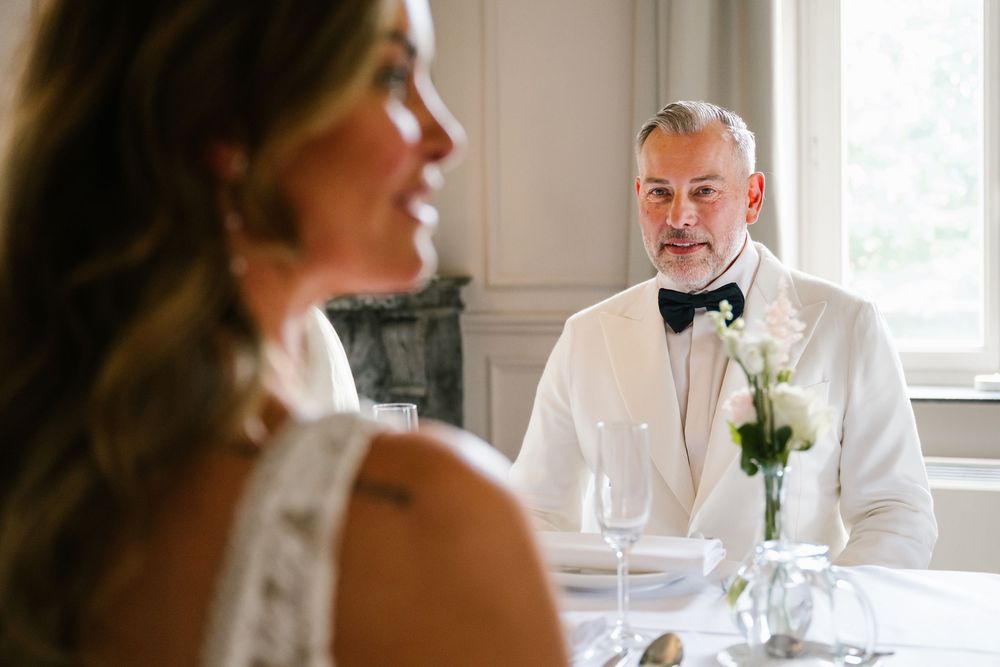Elegant wedding reception scene with white table settings and natural window light in a refined indoor space.