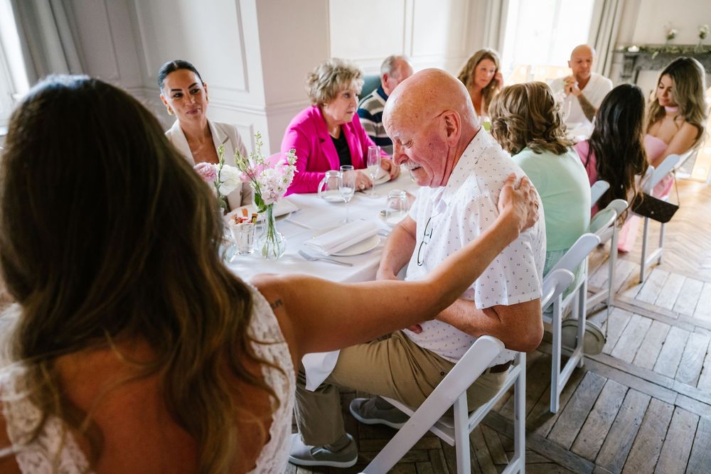 Wedding guests gather at long tables decorated with white linens and floral centerpieces for an elegant outdoor celebration.