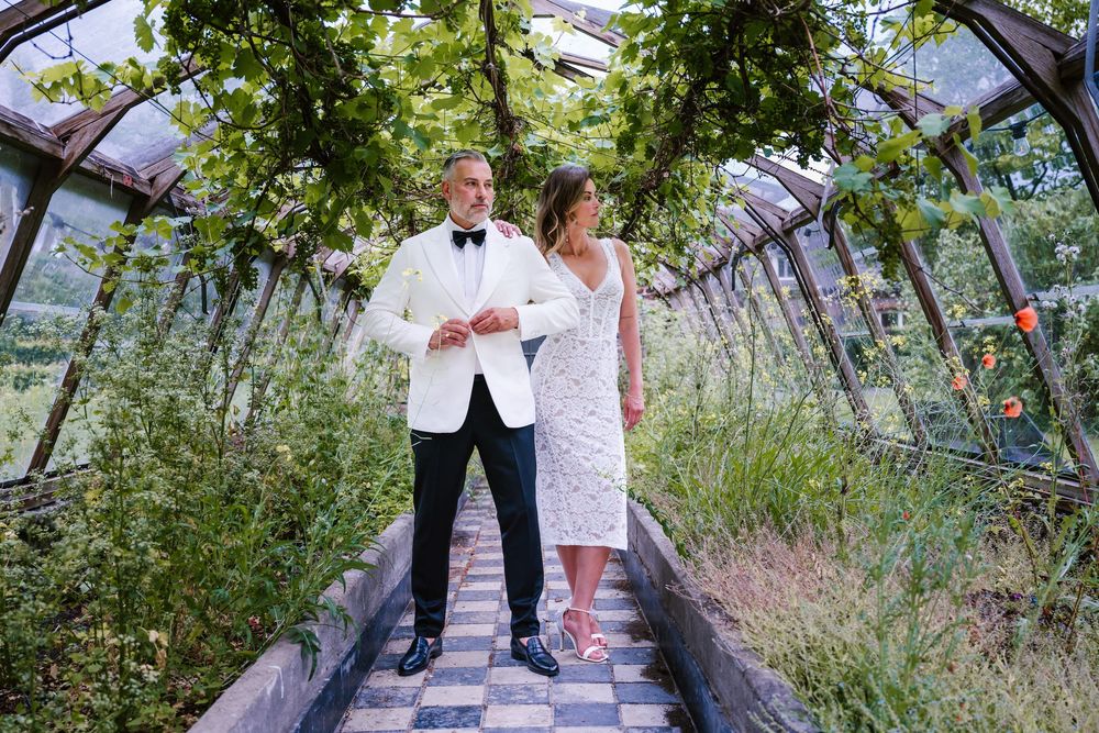 Wedding couple poses in a greenhouse tunnel with lush greenery overhead.