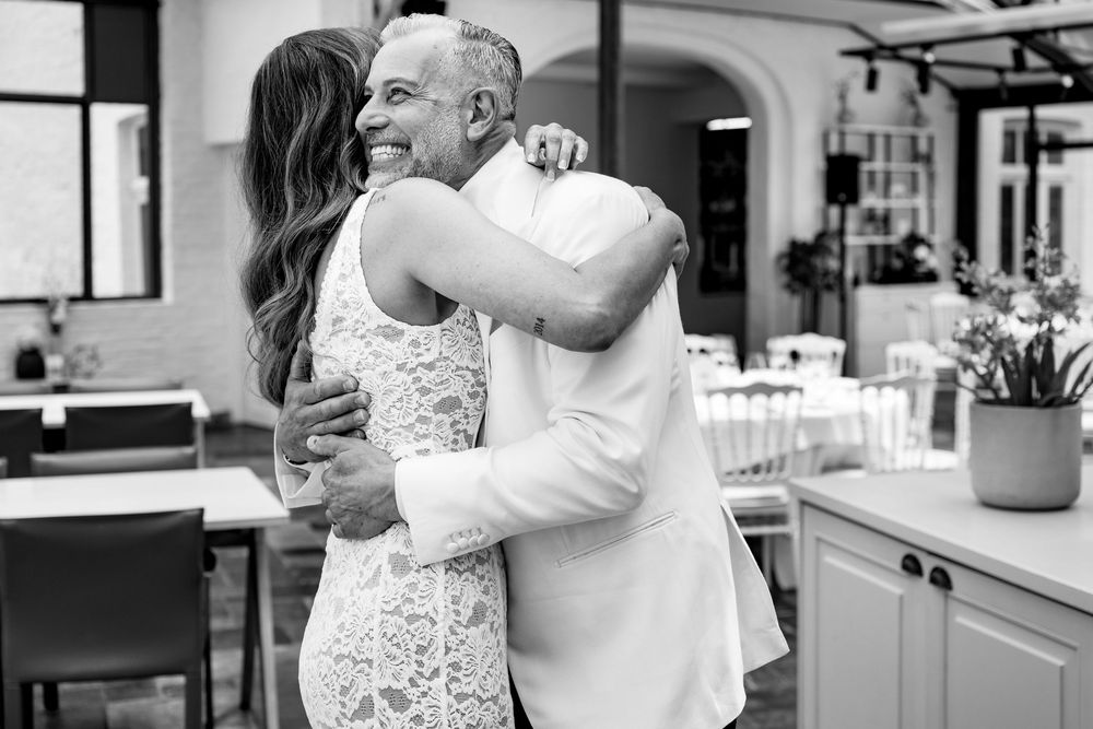 Black and white candid photo showing a warm embrace during a bright indoor celebration.