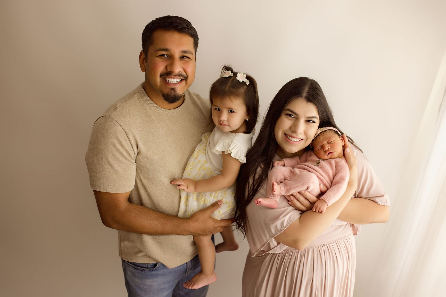 Family portrait of four people wearing beige and pink clothing against a light colored backdrop.