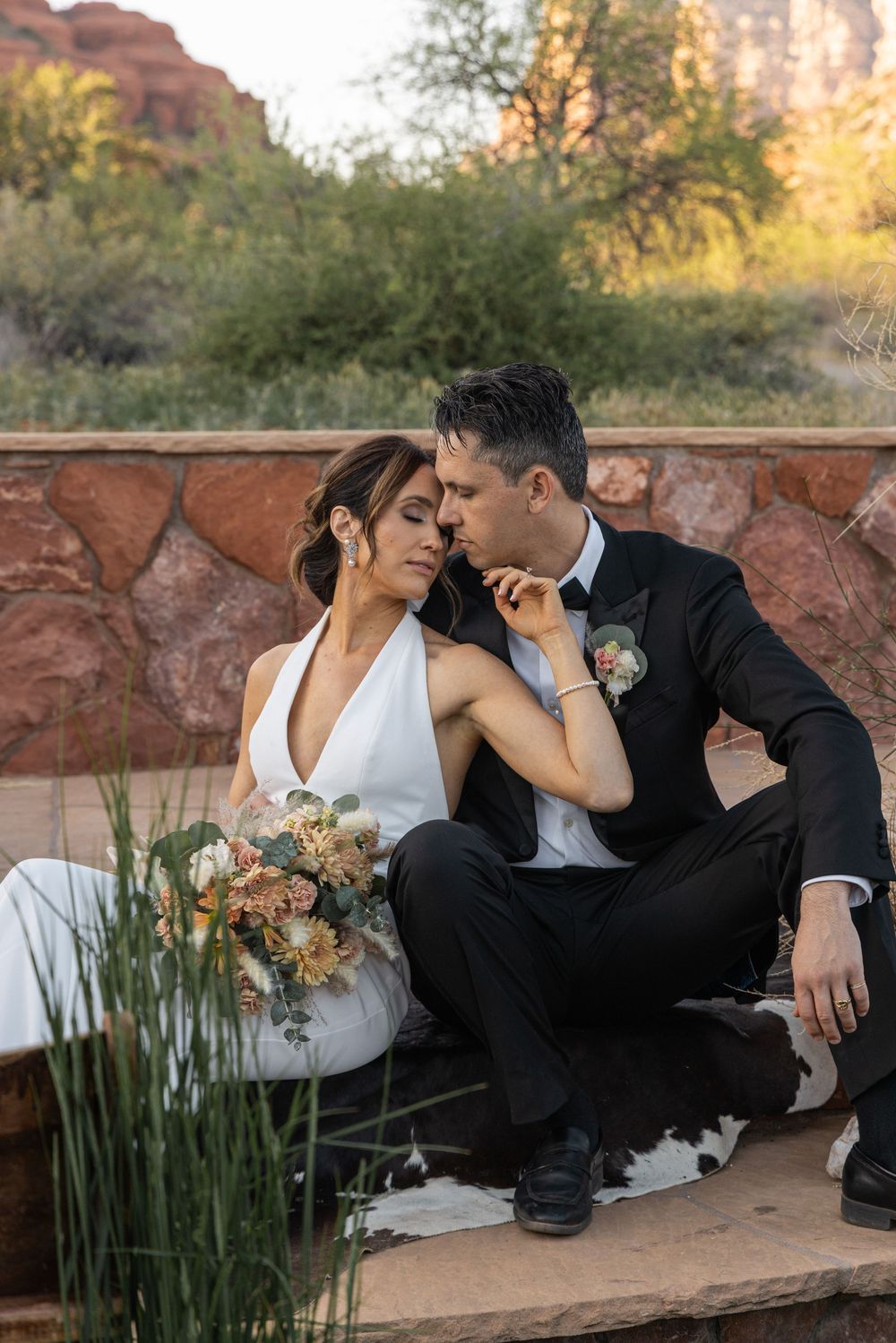 A romantic wedding couple sits together on stone steps at dusk with desert landscape and golden light in background.