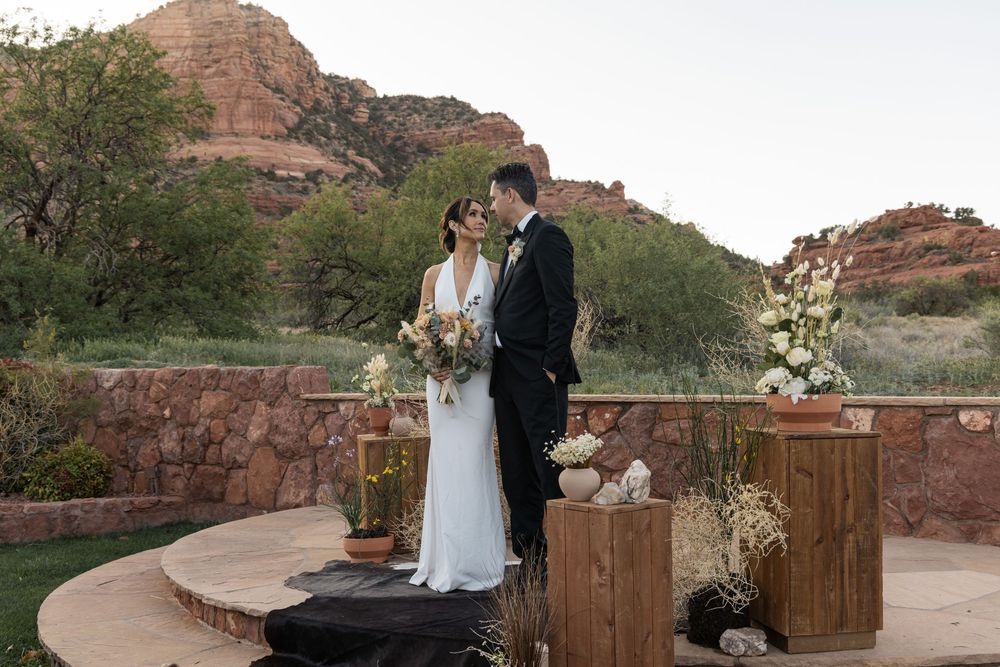 A couple shares a moment during their outdoor wedding ceremony against red rock formations at sunset.