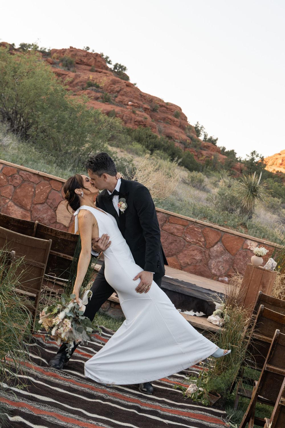 A couple shares a romantic dance pose at sunset against red rock formations in an outdoor desert setting.