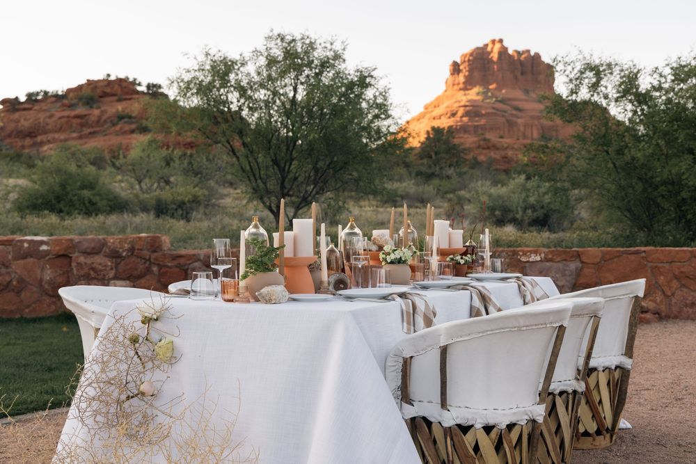 Elegant outdoor dining table set with white linens and decor against stunning red rock formations in Sedona at sunset.
