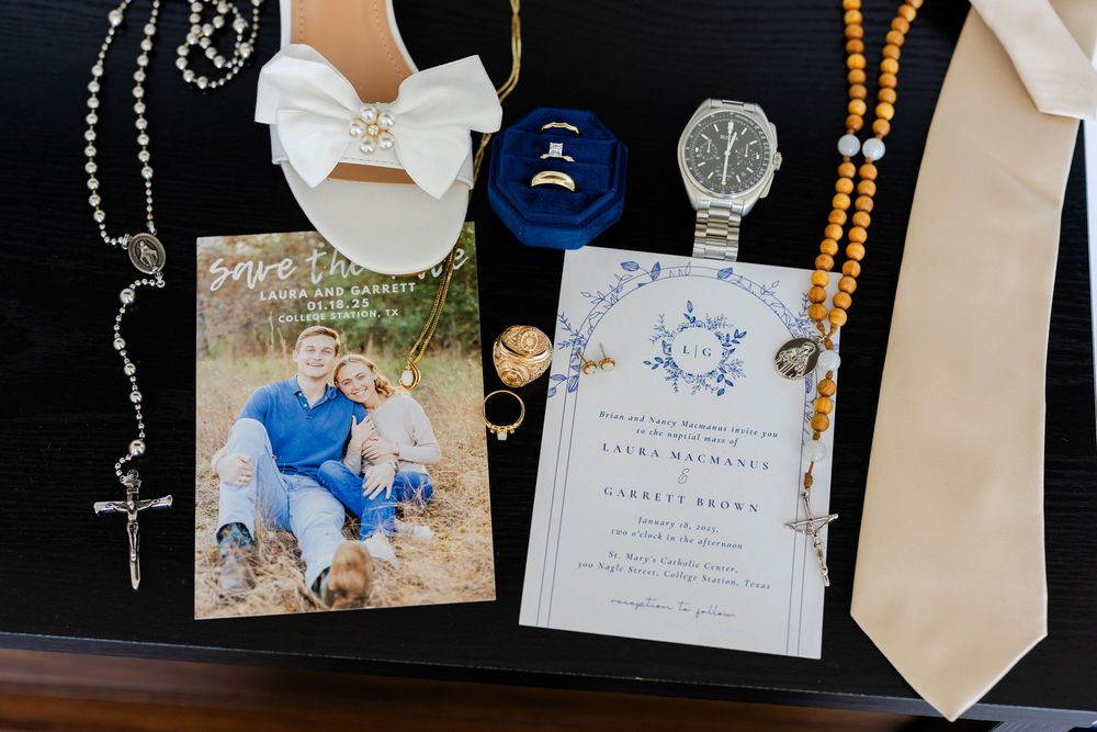 Wedding accessories including a rosary, bow tie, invitation cards, photos and a wristwatch arranged on a dark surface.
