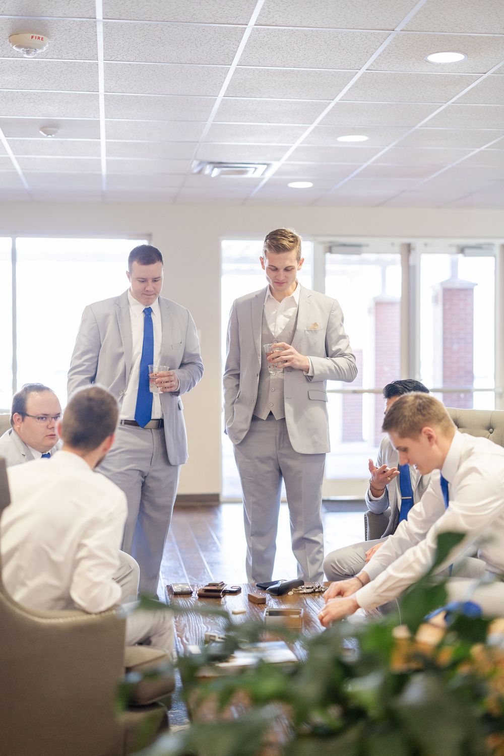 Groomsmen in gray suits gather around a table during wedding day preparations.