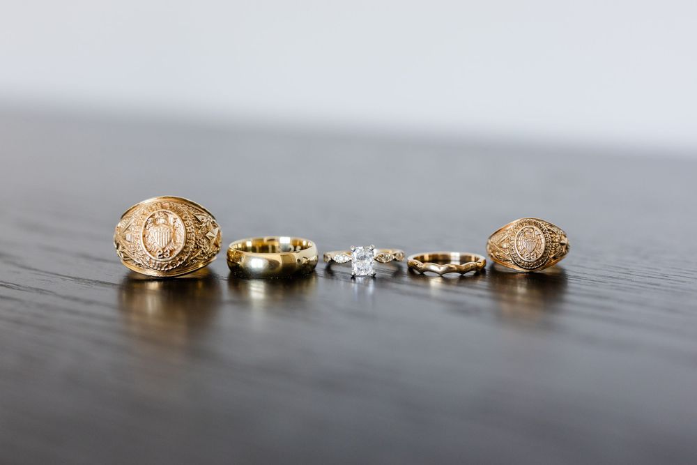 Wedding rings and class rings arranged on a dark wooden surface.