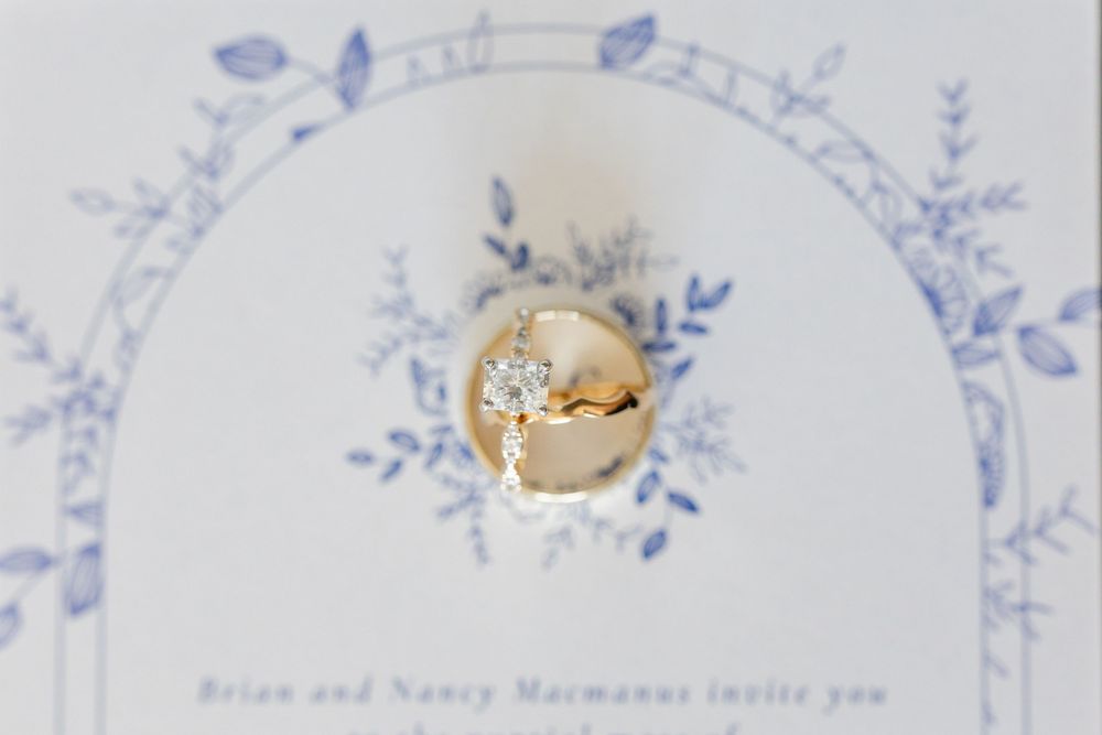 Gold engagement ring photographed on blue and white floral wedding invitation design.