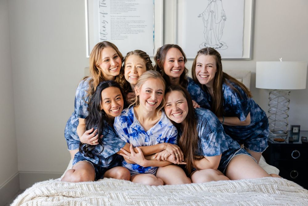 A group wearing matching blue floral robes pose together on a bed during wedding preparations.