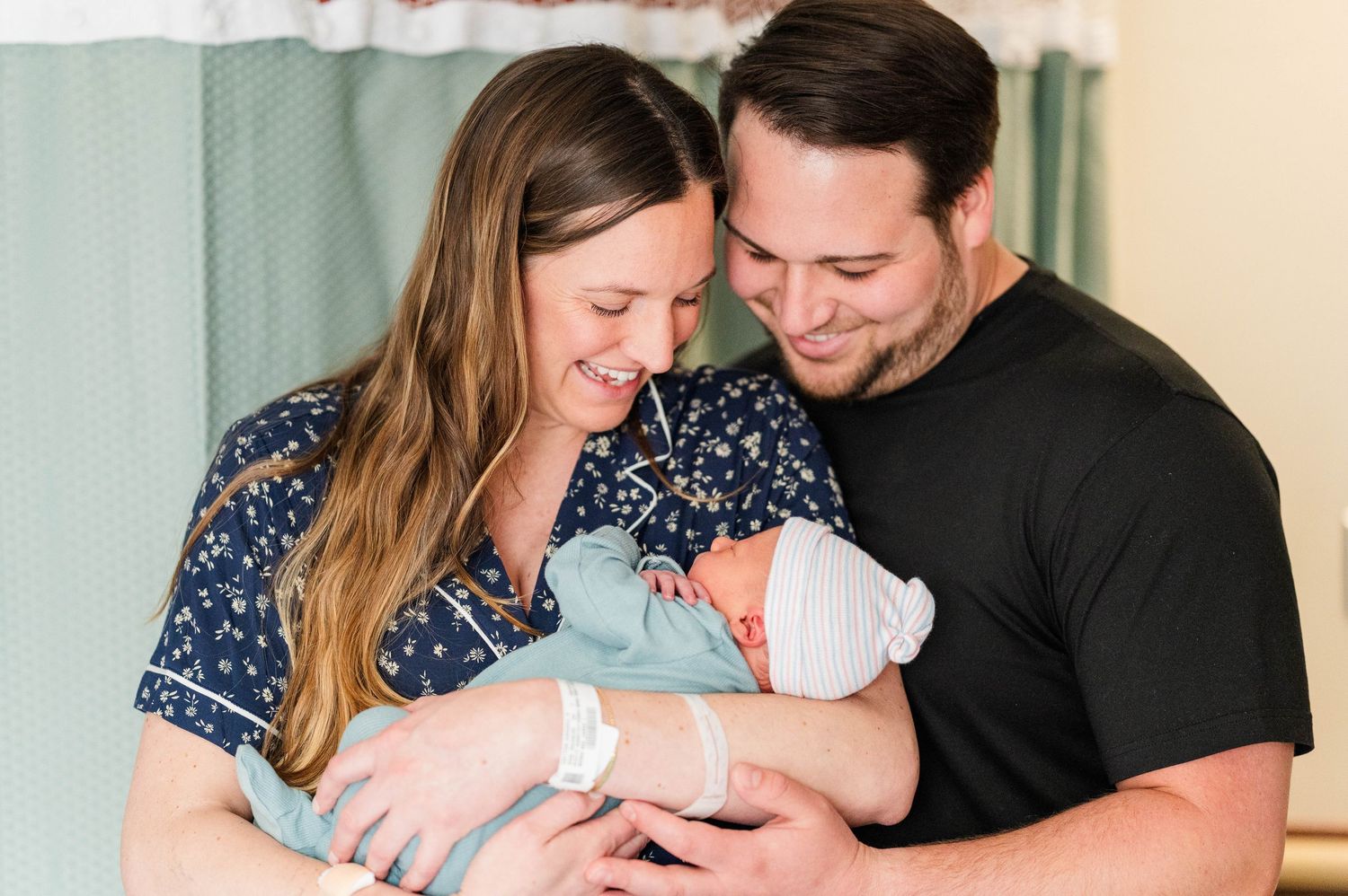 Couple smiling tenderly while holding newborn twin babies wrapped in soft blue blankets.