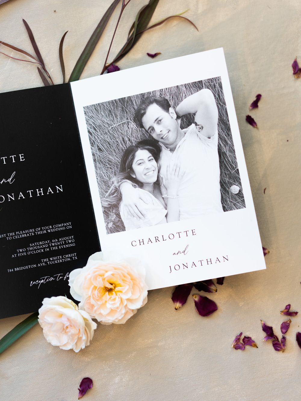 Wedding invitation with botanical elements featuring black and white portrait photo alongside blush roses and purple petals.