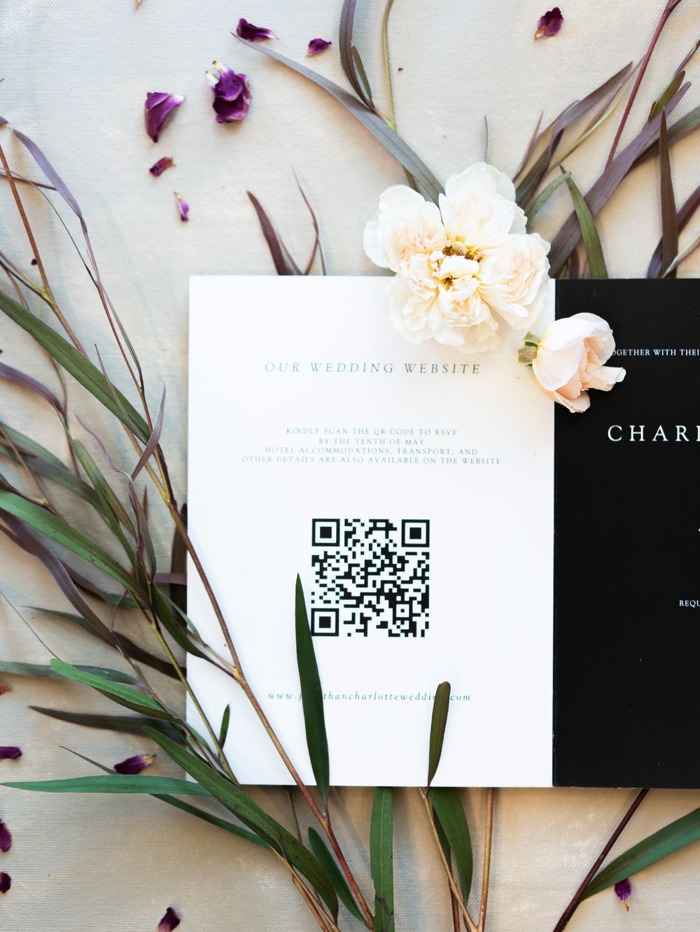 Wedding invitation with QR code displayed among white flowers and green eucalyptus leaves on light background.