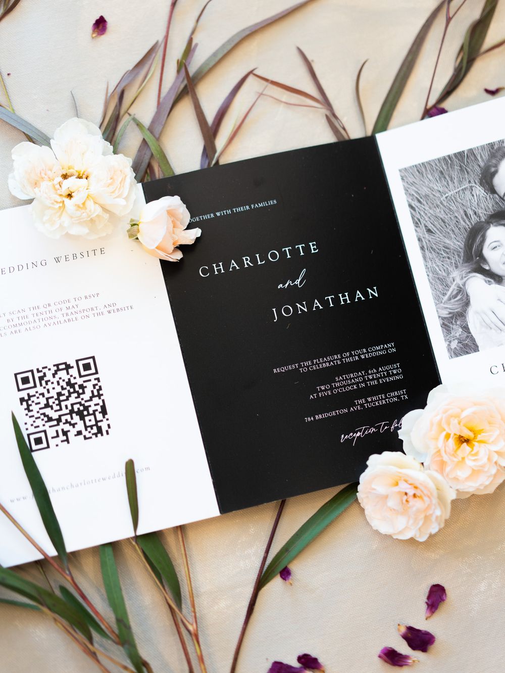 Elegant black and white business cards displayed with peach-colored carnations and purple petals on a cream background.