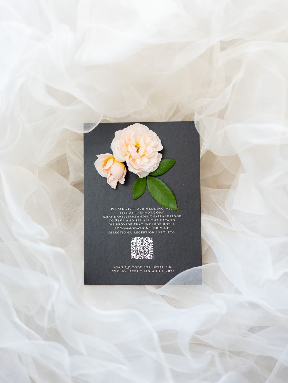 Elegant wedding invitation card with peach roses on dark gray background and QR code against white tulle fabric.