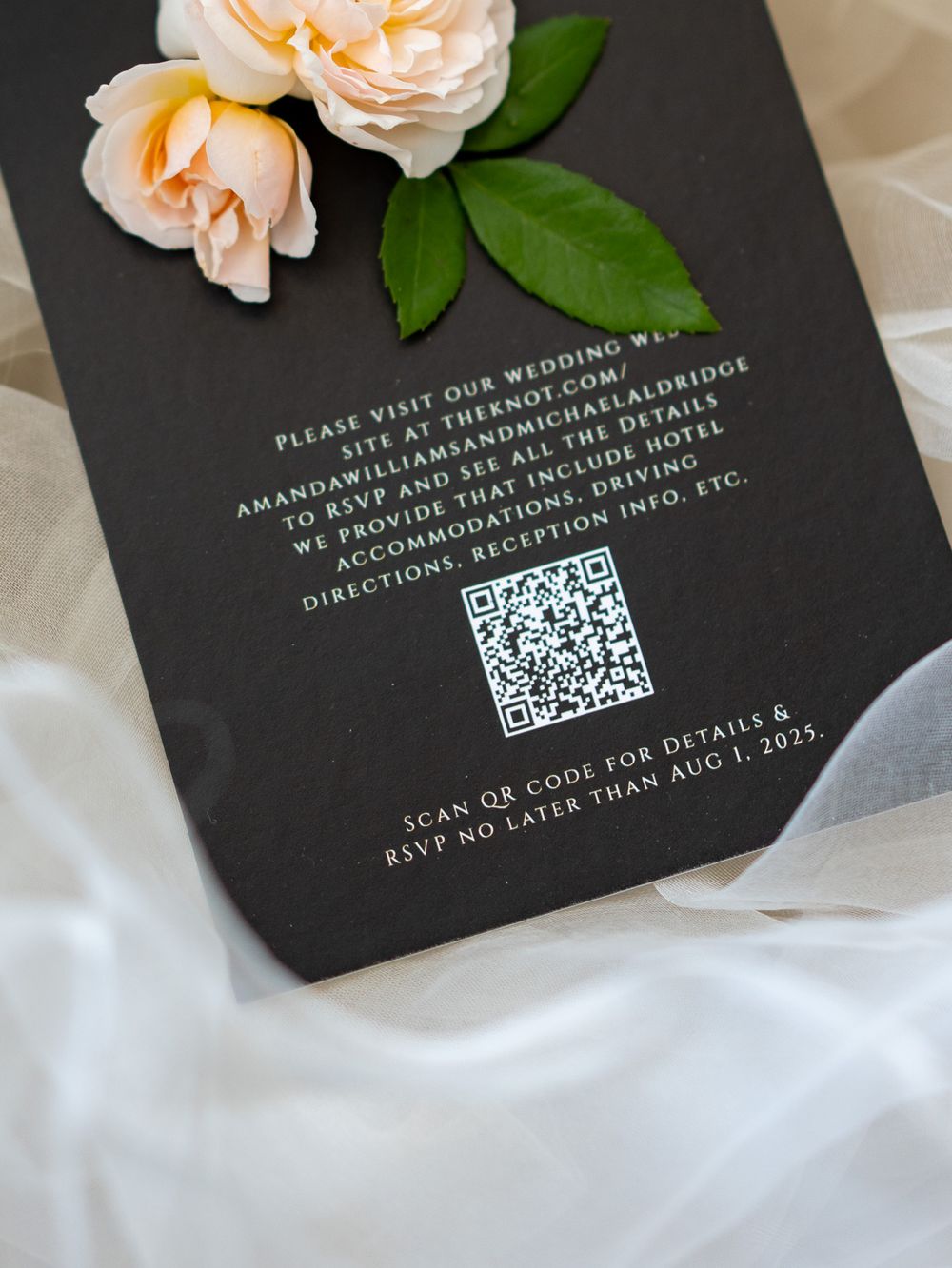 Black wedding invitation cards with QR codes and peach-colored roses on white fabric create an elegant flat lay design.