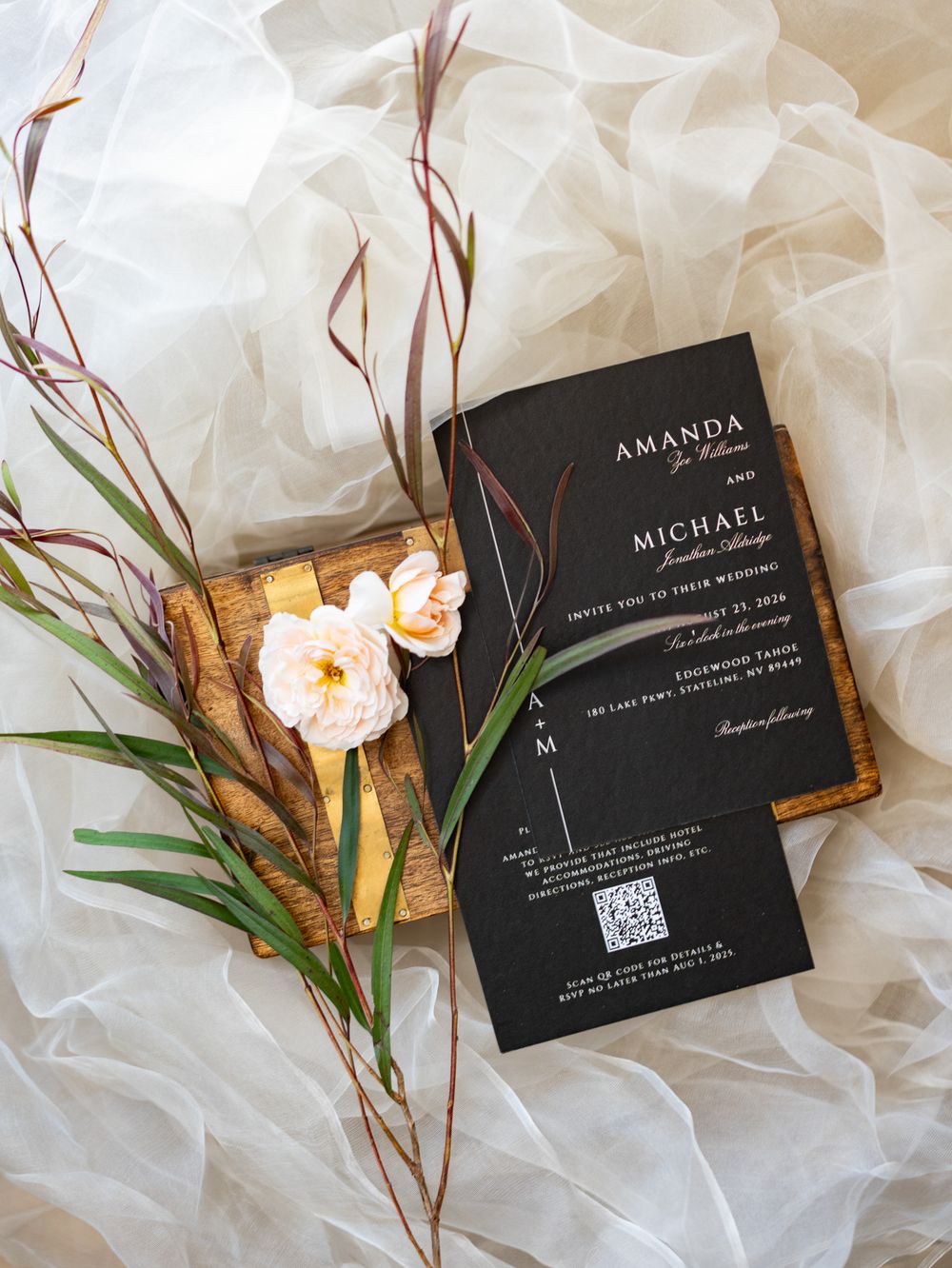 Black matte wedding invitations displayed on white tulle fabric with delicate floral and botanical accents.