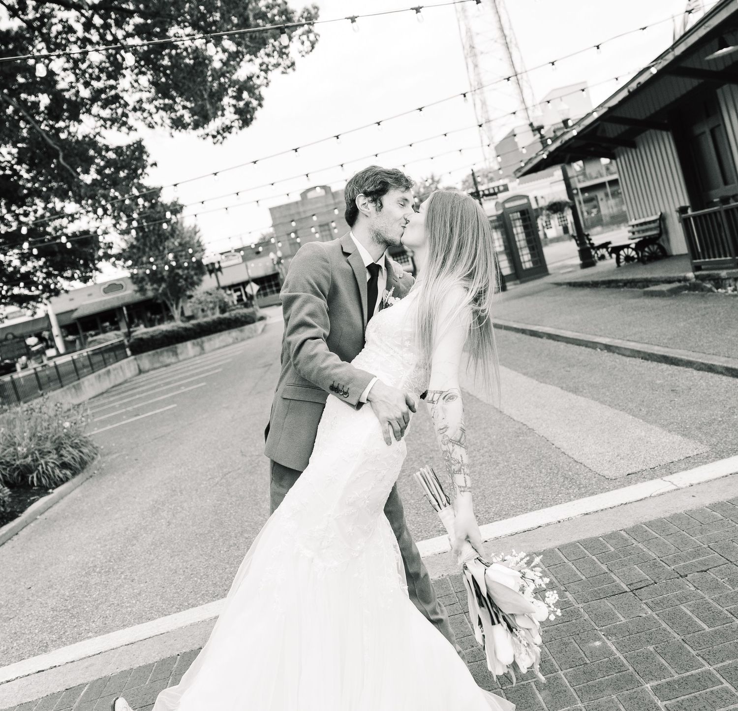 A romantic black and white wedding moment captured on a brick pathway with string lights overhead.