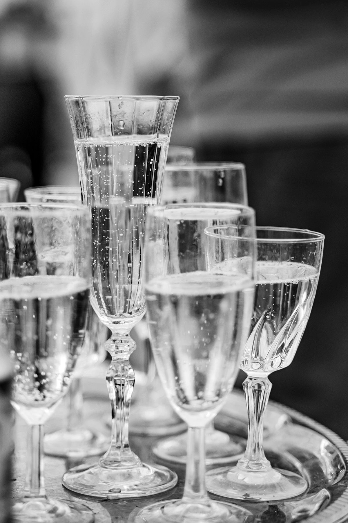 Svartvit detaljbild från bröllop – champagneglas med bubbel i olika modeller vackert uppställda på bricka. Bröllopsinspiration för dukning.