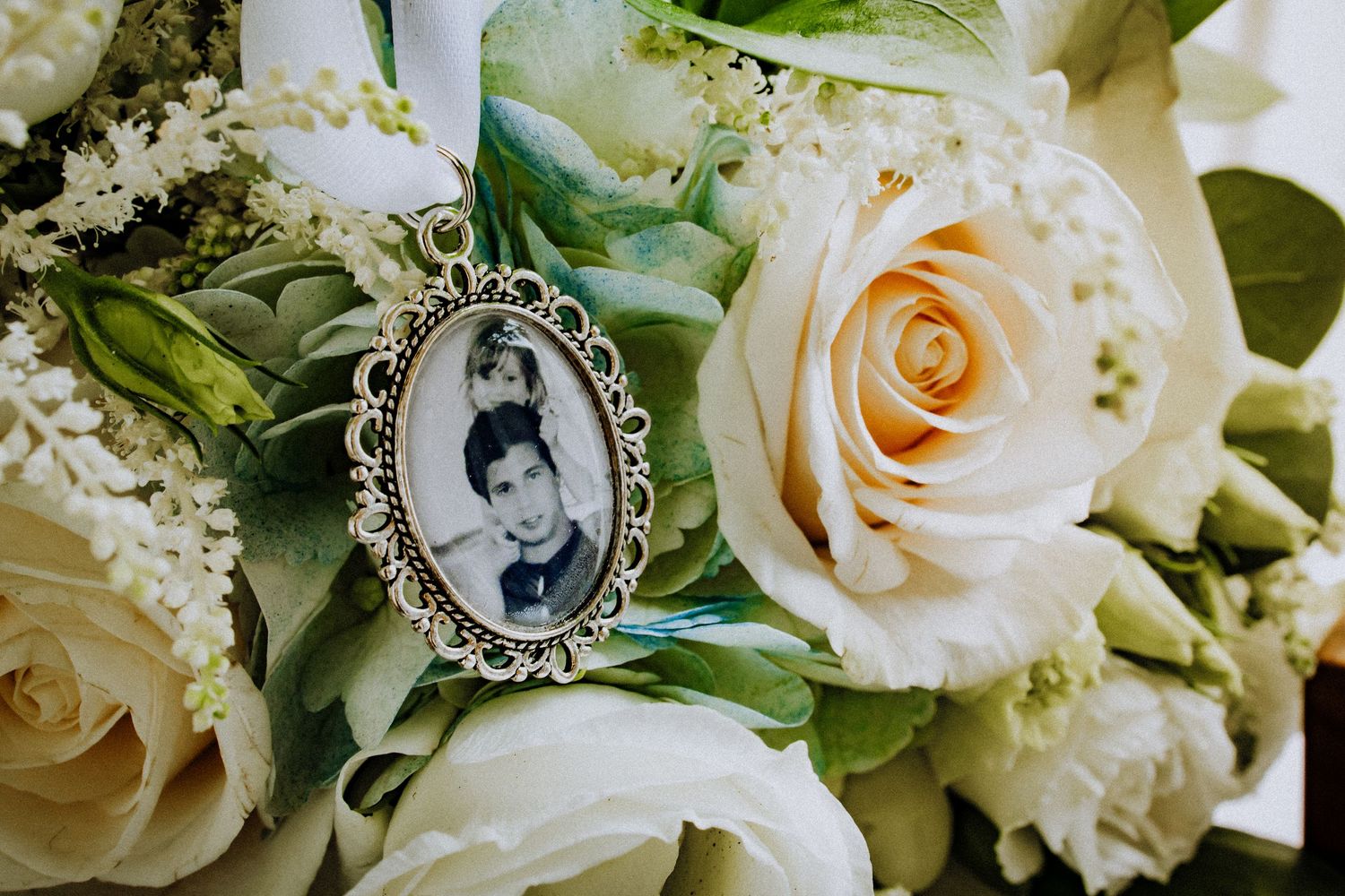 An antique silver brooch with an old photo nestles among cream roses and greenery in an elegant bouquet.