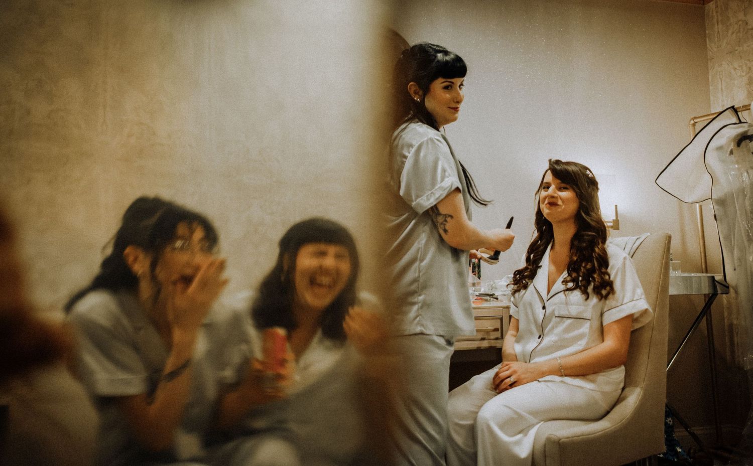 A warm-toned candid shot shows laughter and joy during wedding preparations in a vintage-styled room.