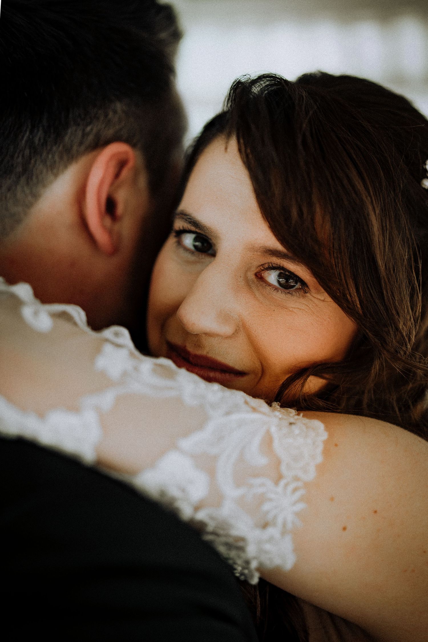 Close-up intimate wedding portrait showing a loving moment in natural light with lace dress details and moody shadows.