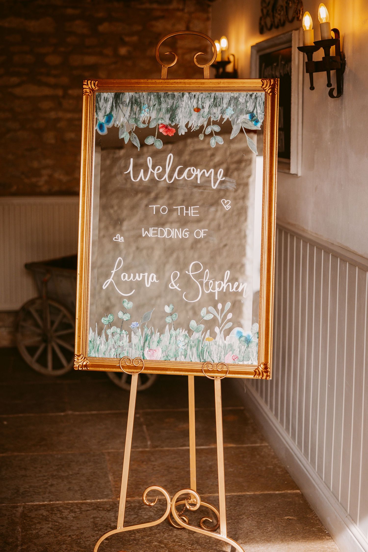 Elegant gold-framed welcome sign on an easel with floral accents and white calligraphy for a wedding celebration.