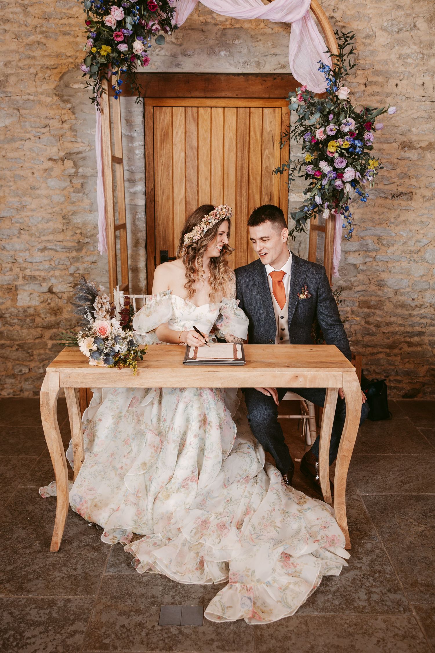 A wedding celebration at a rustic venue with wooden doors decorated with floral arrangements and flowing fabric.