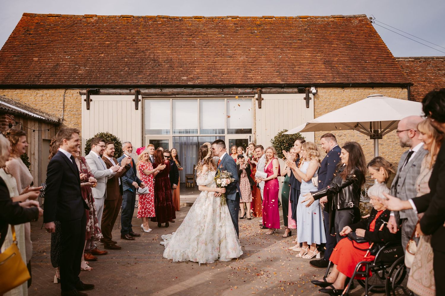 Guests gather in rustic courtyard during a wedding celebration at a historic barn venue with red tiled roof.
