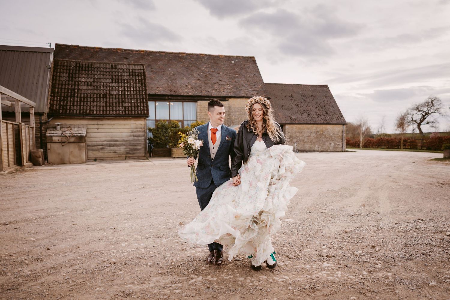 A couple enjoying a candid moment in their wedding attire outside a rustic barn venue on an overcast day.