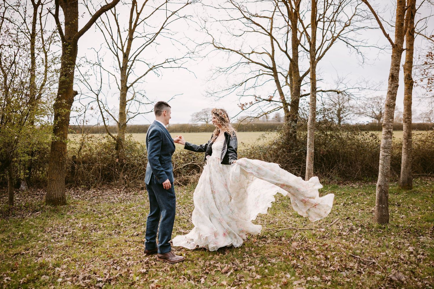A romantic wedding couple poses in a wooded area with the bride's dress flowing elegantly in the breeze.