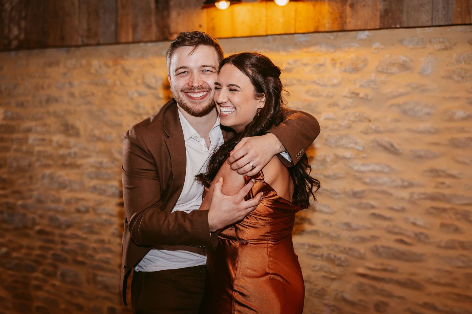 A joyful couple shares an intimate moment while embracing against a rustic brick wall.