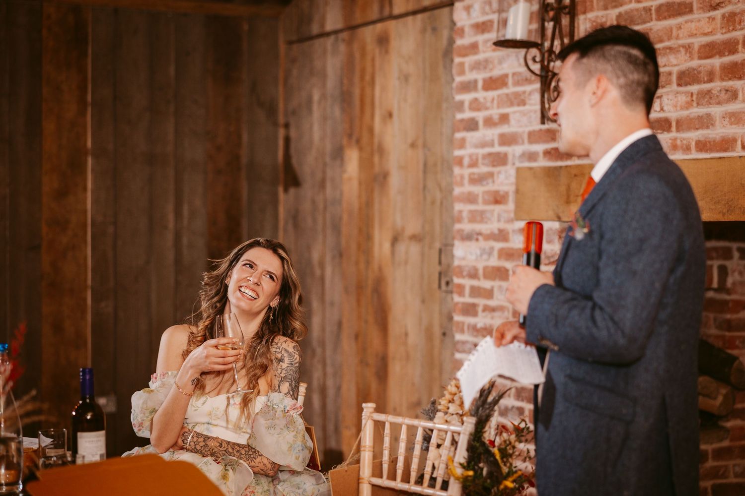 At a rustic venue with brick walls, two people share a heartfelt moment during a wedding toast.