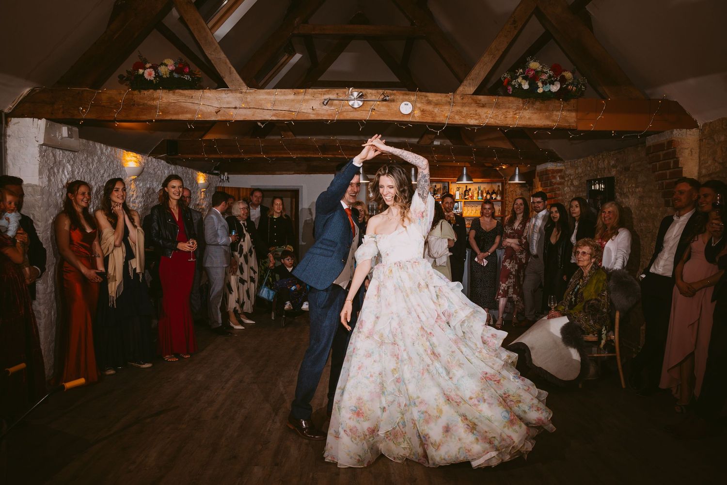 A couple performs their first dance surrounded by wedding guests in a rustic barn venue.