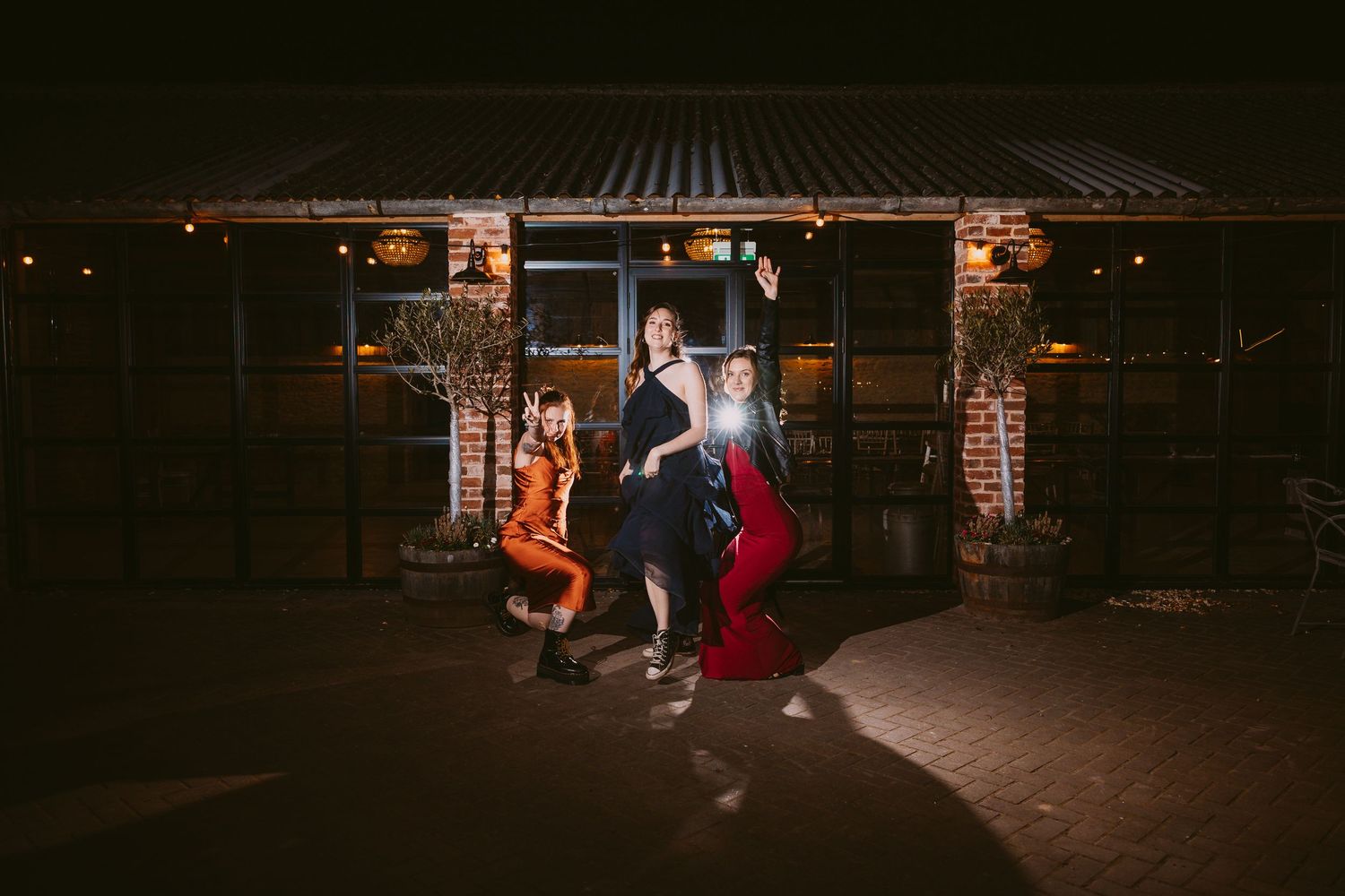 A group poses in vintage 1950s style attire outside a darkened rustic building with warm lighting.