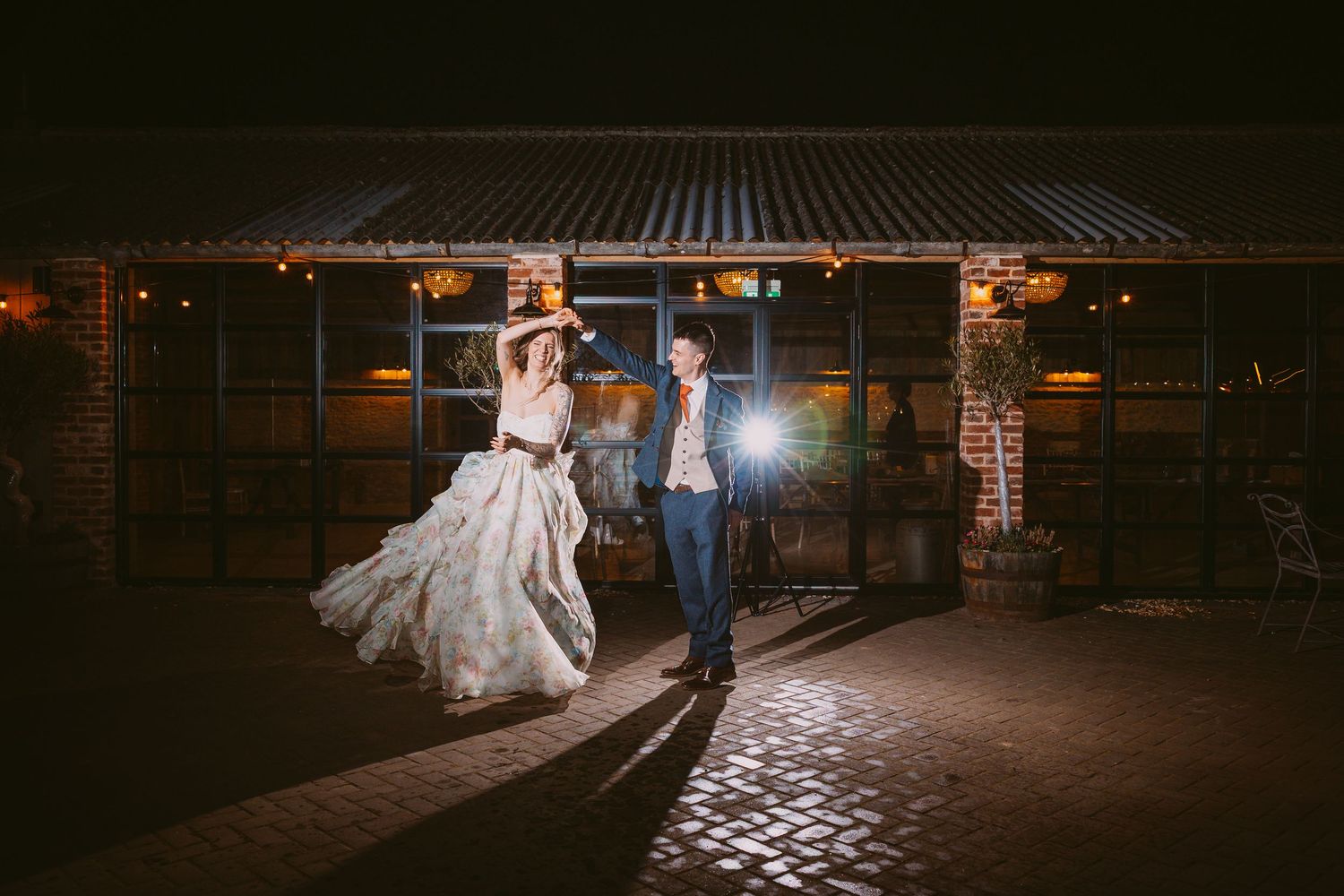 A couple dances under evening lights outside a rustic brick and metal venue.