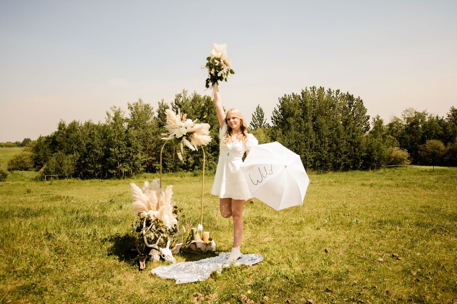 Rolling grassy meadow with white fabric and flowers creating a romantic outdoor setting at golden hour.