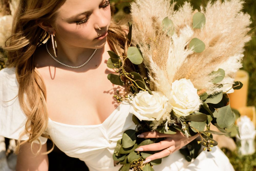 A graceful bride in a white dress holds a romantic bouquet of ivory roses and pampas grass with eucalyptus.