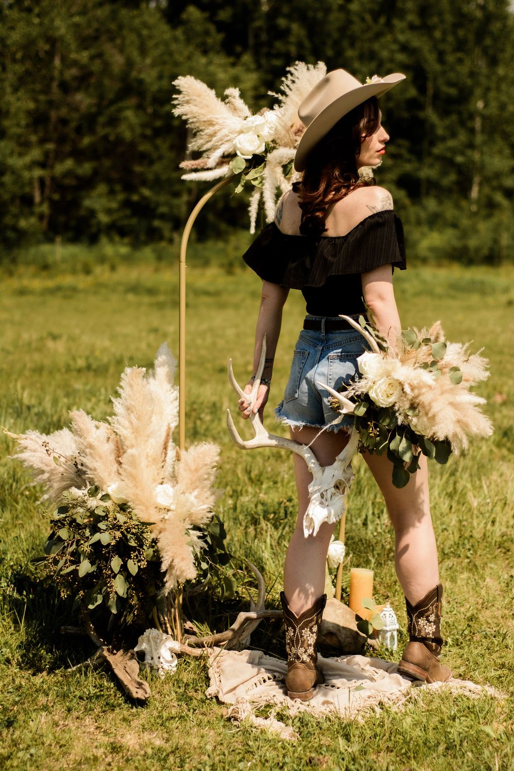Boho-styled outdoor setting with pampas grass arrangements and rustic decorations on grass.