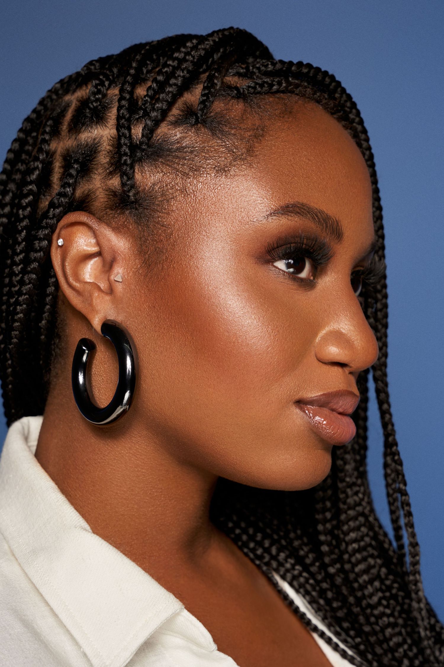 Side profile beauty shot showcasing intricate braids and large black hoop earrings against blue background.